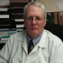 Dr. John Thomas sits in an office while wearing a white lab coat.