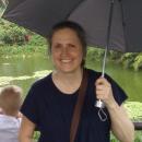 Dr. Christina Bueno standing with an umbrella and children in the background looking at a pond