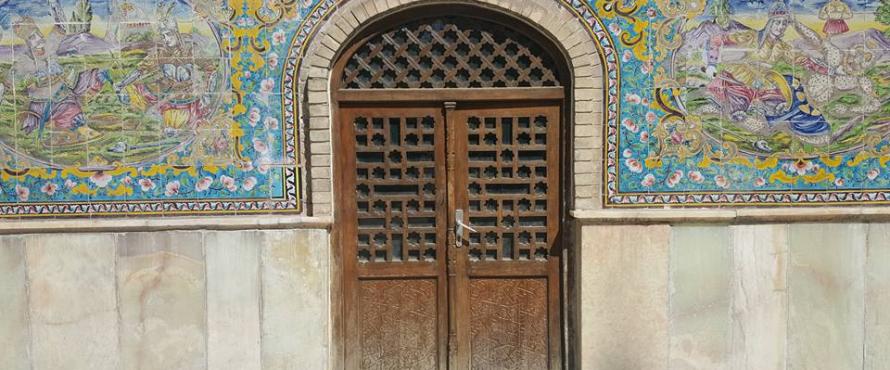 A carved wooden double door surrounded by painted tiles at a location in Iran