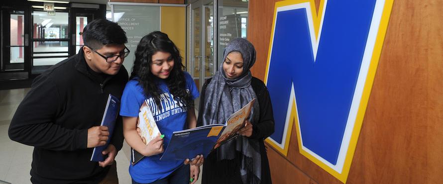 One male and two female students look at a Northeastern brochure