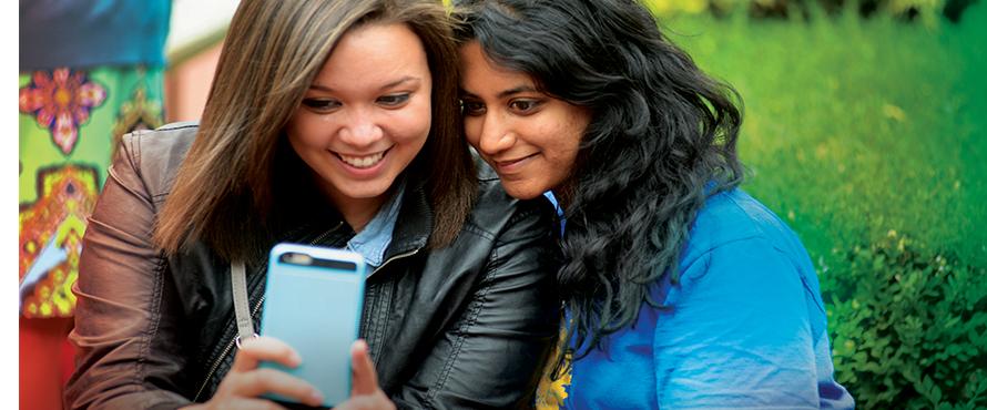 Two female students sit closely together to take a selfie photo on a mobile phone