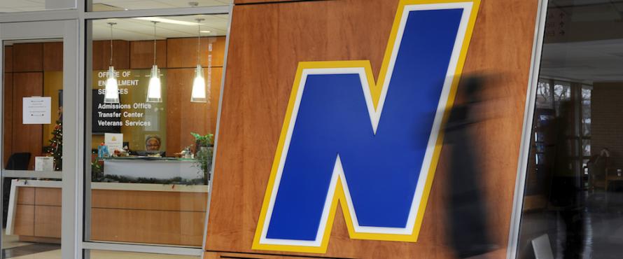 Blurred students walk past the Northeastern Illinois University "N" logo.