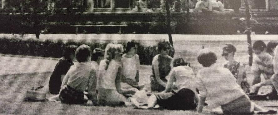 Members of the Class of 1967 sit in a circle on the lawn outside of the Sachs Building
