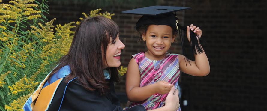 Graduate in gown with daughter wearing cap, both smiling.