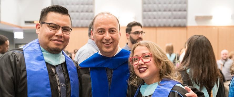 Two men and a woman at the Master's Hooding Ceremony pose for a picture