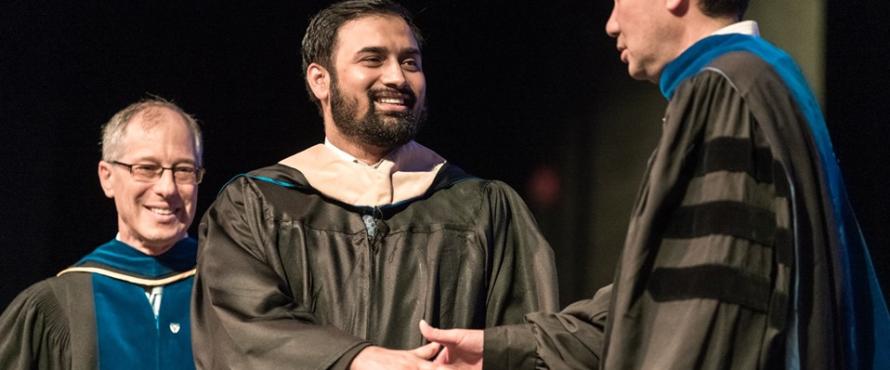 A man shakes a graduate's hand at the Master's Hooding Ceremony