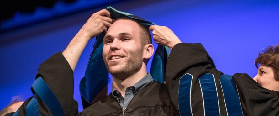 Two people drape a hood over a male graduate's head at the Master's Hooding Ceremony
