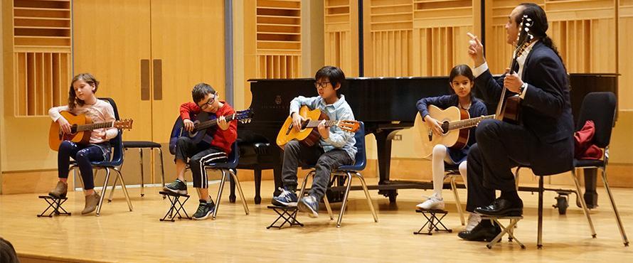 Students play the guitar on the Recital Hall stage.