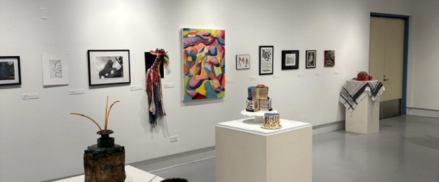 Gallery view of art show with sculptures on pedestals and wall hanging artwork including photography, painting and designed posters