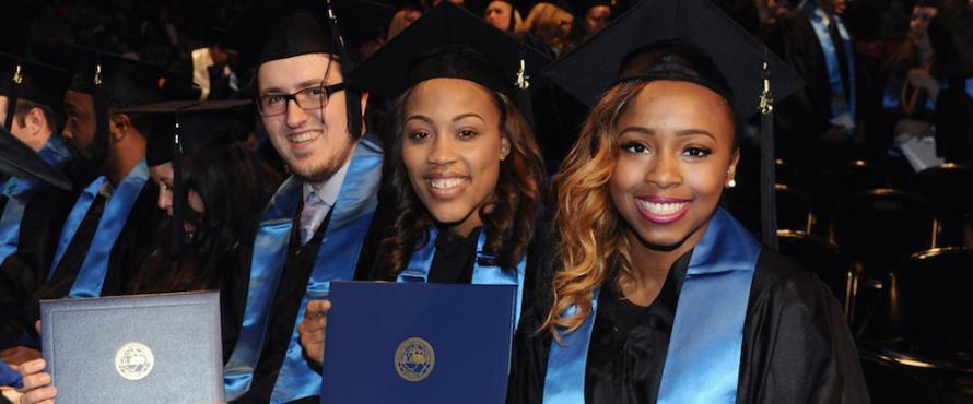 From left to right, a male and two female graduates holding diplomas and smiling