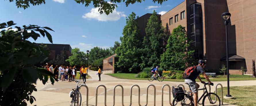 Daytime view of the Univesity Commons with the Library in the background to the right, a tour group standing to the left and a bicyclist in the foreground