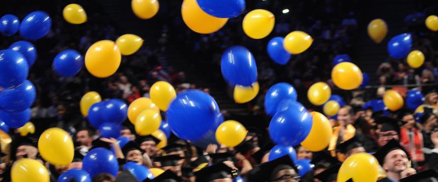 Blue and yellow balloons fall from the rafters at the UIC Pavilion during NEIU Commencement