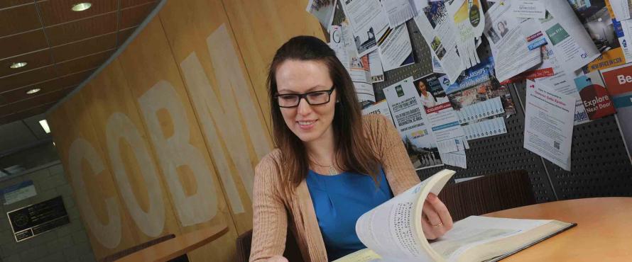 Accounting student Anna Davydova sitting at a table and turning the pages of a book