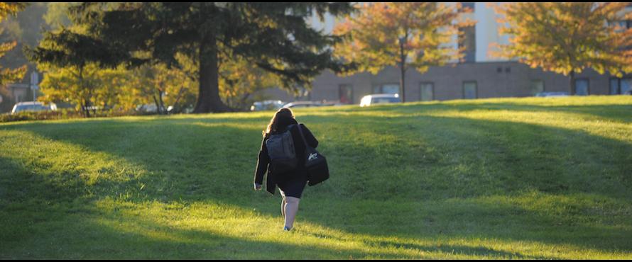 A woman is seen from behind as she walks across the grassy area east of The Nest