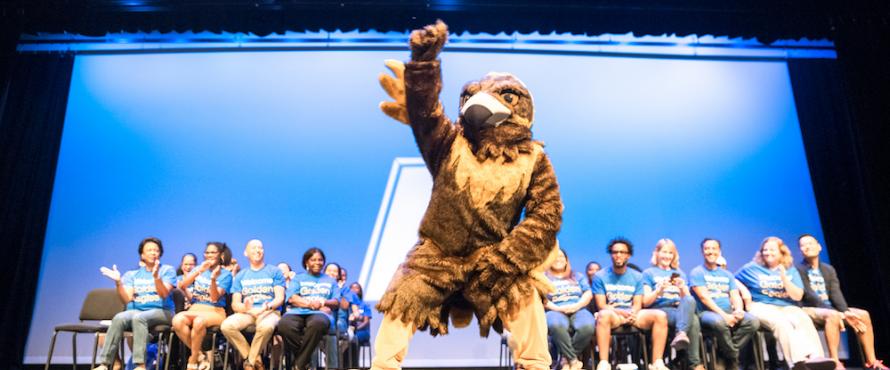 NEIU mascot Goldie the Golden Eagle raising a wing on the Auditorium stage