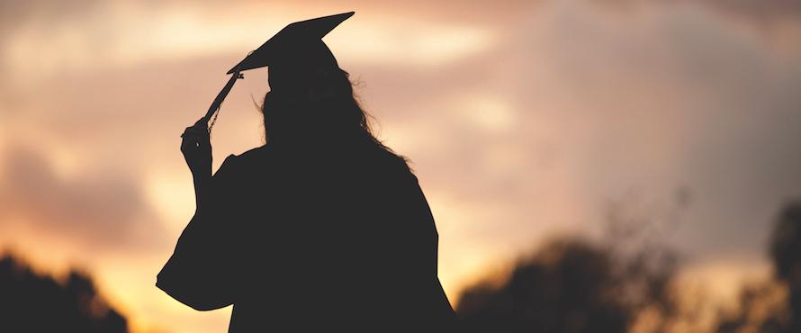 A female graduate wearing gown and mortarboard in silhouette against a sunset sky