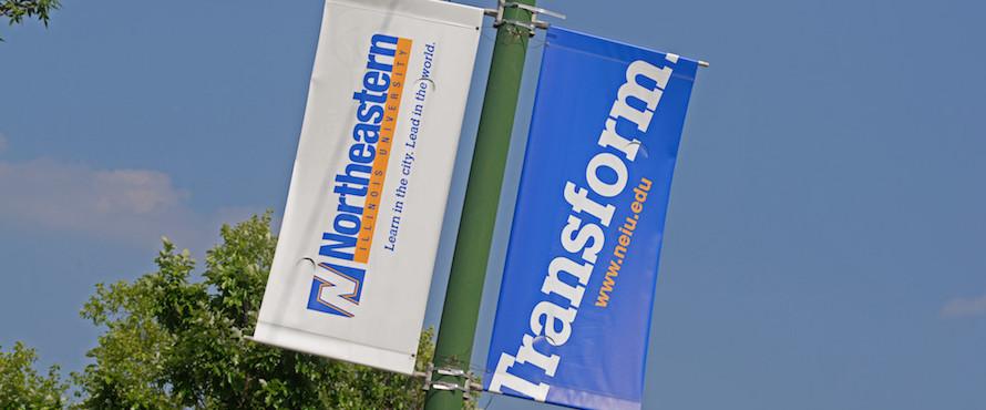 Two banners hang from street light poles; one reads Northeastern Illinois University, the other reads Transform