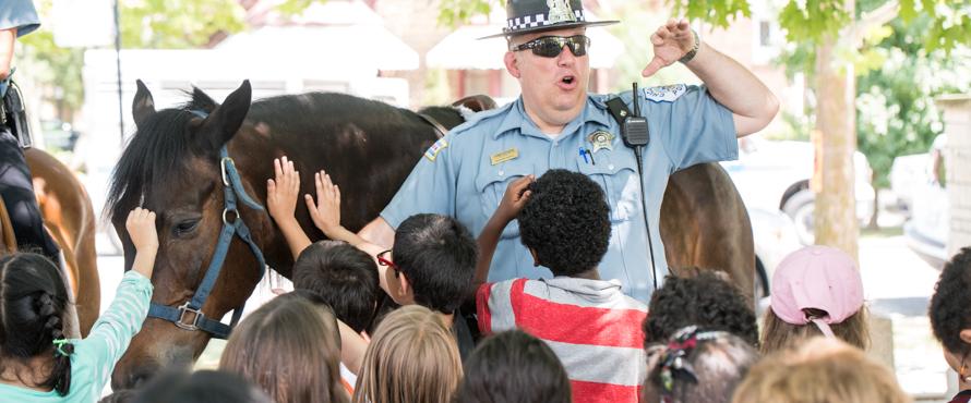 A Chicago Police Officer answers questions while standing in front of a police horse.