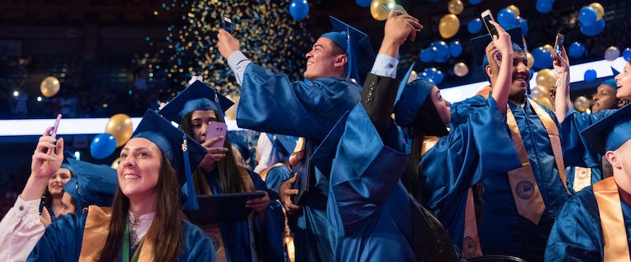 Graduates wearing blue caps and gowns celebrate at Commencement