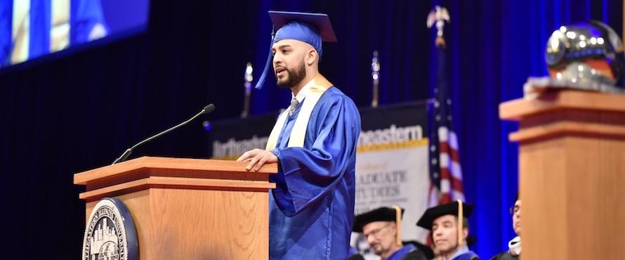 Michael Angelo Ortega delivers the student speech during Commencement while wearing a blue cap and gown.