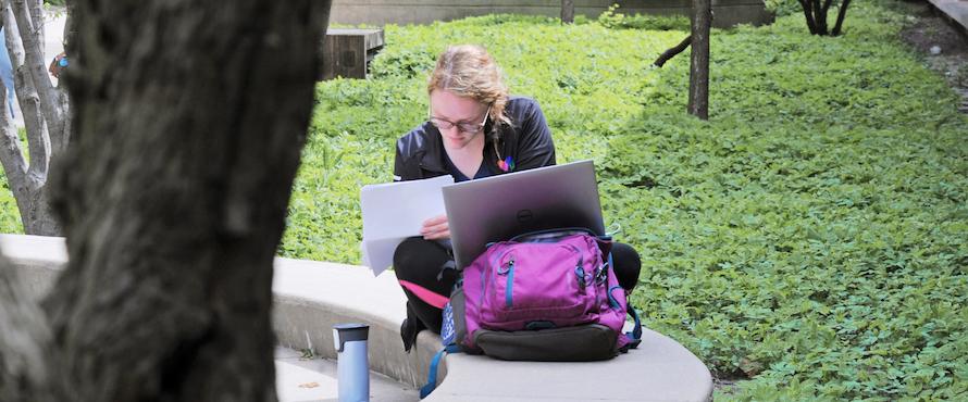 A woman works on her laptop at a table outside.