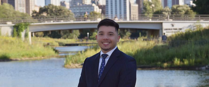 A photo of Julio E. Arreola in a suit and tie standing in front of the Chicago skyline.