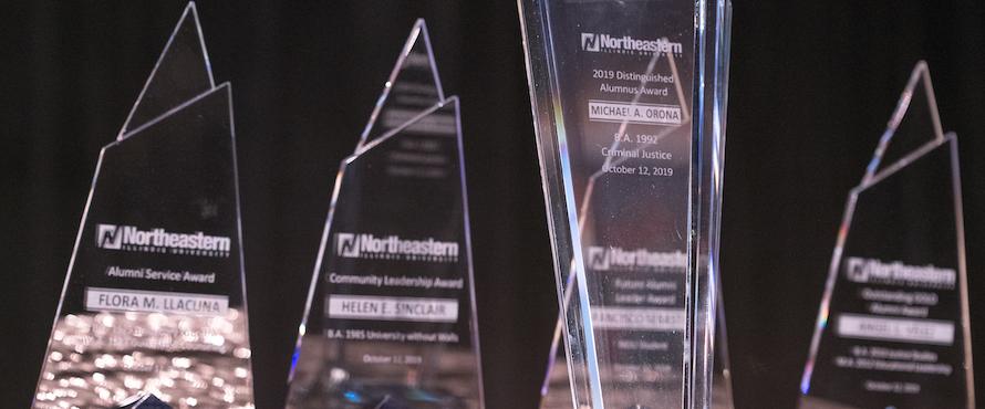 Four triangular, glass Alumni Awards against a black background