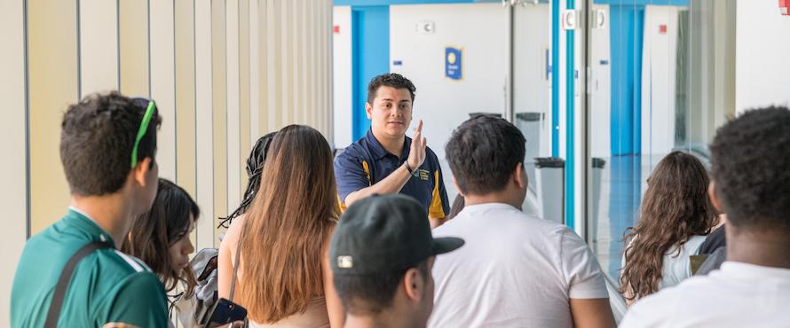 An instructor stands at the head of a classroom addressing a group of students