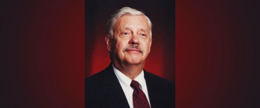 Photo of Dr. David F. Unumb in a dark suit and tie with a red gradiant background