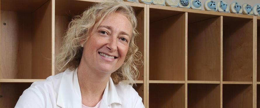 Photo of Pam Geddes in a white shirt with wooden cube shelves in the background.