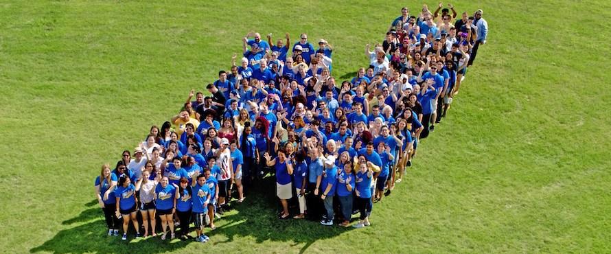 NEIU's Flying N logo is formed by a large group of people outdoors on the University Commons