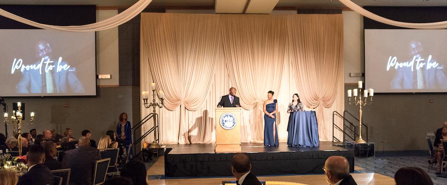 Three people stand on a stage at the Golden Gala