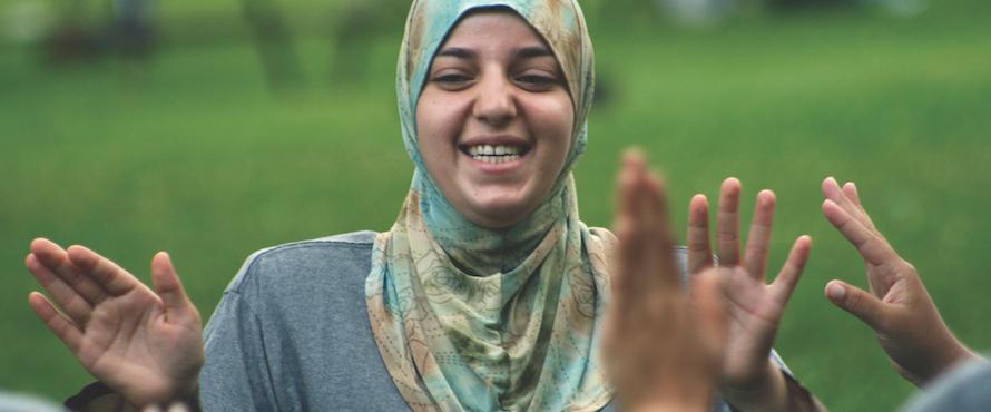 A student outdoors wearing an NEIU shirt and a headscarf smiles 