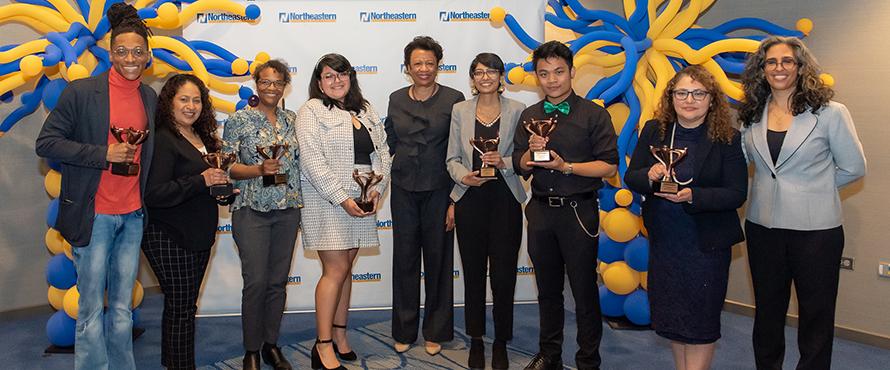 The seven recipients of the inaugural 2022 NEIU President's Inclusive Excellence and Diversity Awards smile and hold their trophies alongside President Gibson and the Executive Director of Equity, Diversity and Inclusion.