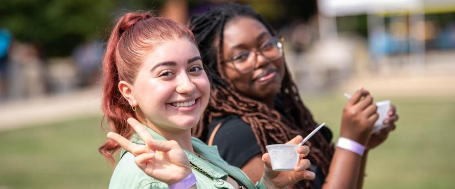 Two students eating a snack outdoors smile as they walk together