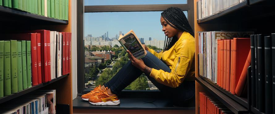 A young woman reading and sitting on a window seat in a library