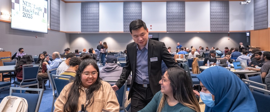 A photo of Chair and Professor of Computer Science Xiwei Wang, Ph.D., standing, talking with students during the 2025 NEIU Eagle Hackathon.