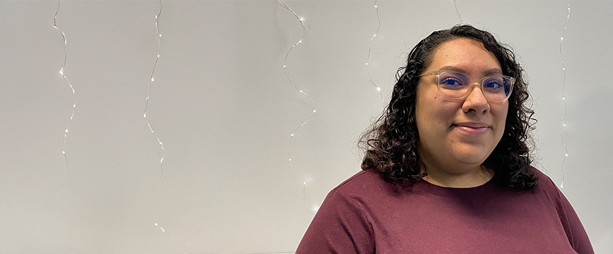A headshot photo of Jaqueline “Jackie” Ortiz-Basave, smiling, standing against a gray background with twinkle lights.