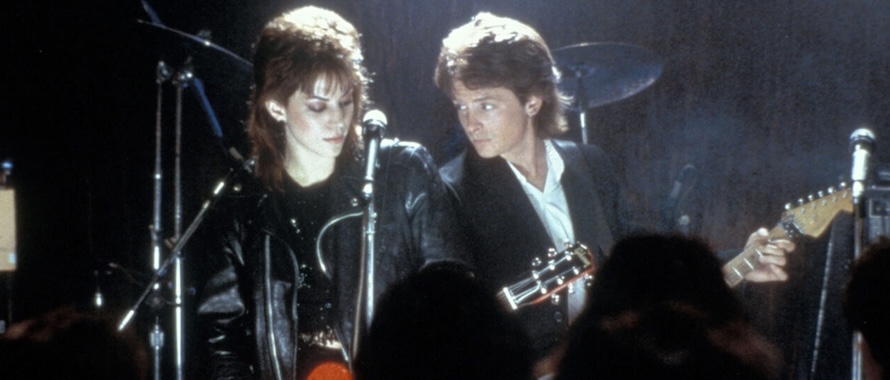 A still image from the film "Light of Day," starring Joan Jett (left) and Michael J. Fox (right), playing guitars, standing near microphones. Image courtesy of Chicago Film Society. 