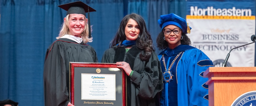 A photo of (from left to right) Northeastern Vice President for Institutional Advancement Liesl Downey, PJ Randhawa and Northeastern President Katrina E. Bell-Jordan, all wearing graduation robes, smiling during the University's December 2025 Commencement. Downey and Randhawa are holding a framed certificate, commemorating Randhawa's speech.