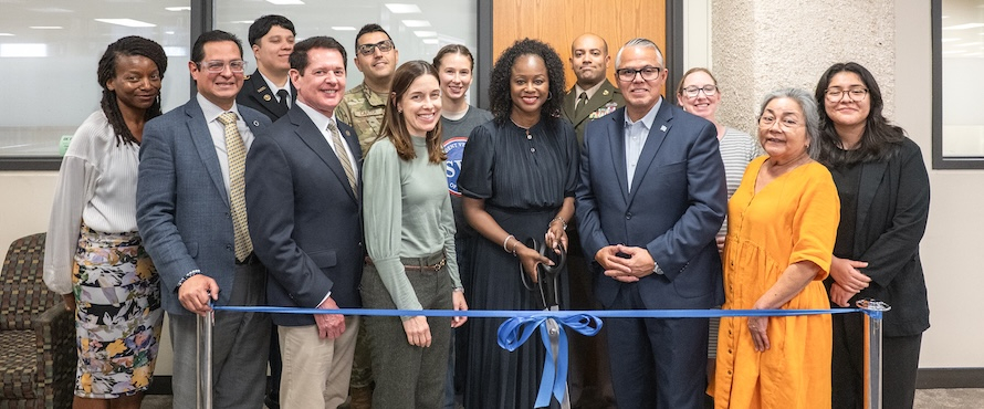 A group photo of Northeastern Illinois University President Katrina E. Bell-Jordan (center, holding a large pair of scissors) surrounded by University administrators, staff, students and guests, standing behind a blue tied ribbon, prior to the opening of the University’s new Veterans Services Center on Oct. 6, 2025.
