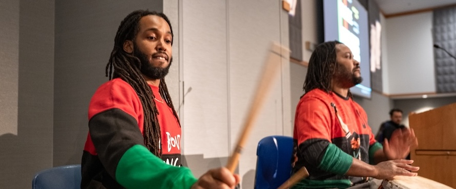 A photo of two people playing drums at Northeastern Illinois University's Alumni Hall.