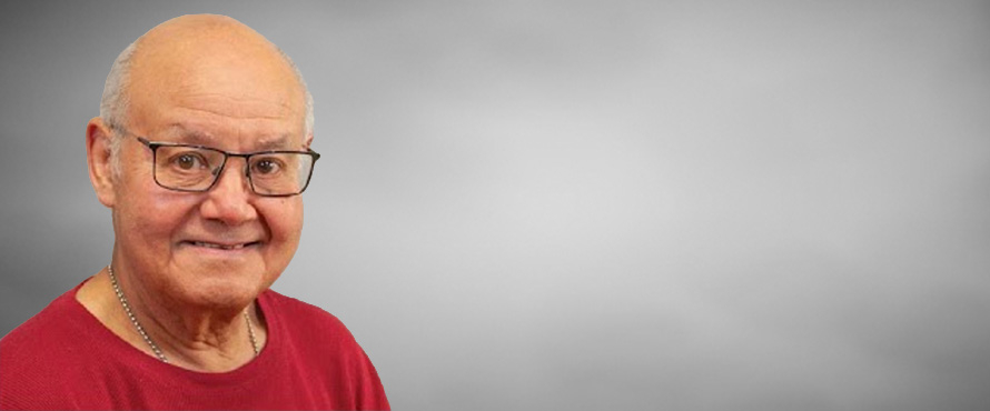 A headshot photo of Joaquin Villegas, Ph.D., smiling, wearing a red T-shirt and black-rimmed glasses. The background is a grey gradient.  