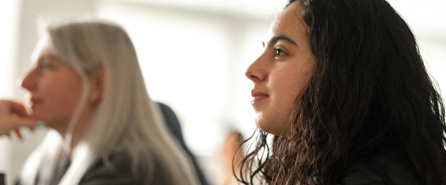 A photo of two people in a classroom looking toward the front of a room, listening to a presentation, during Northeastern Illinois University's annual John S. Albazi Student Research and Creative Activities Symposium.