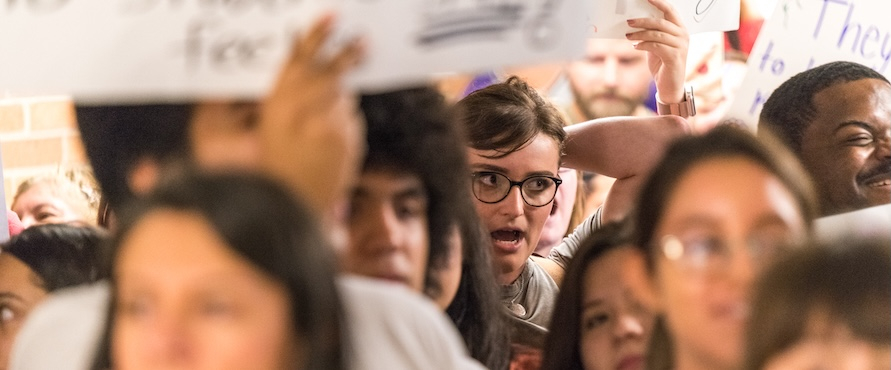 A photo of people gathered holding protest signs. The text on the signs is blurred. 