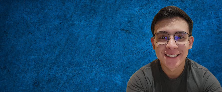 A photo of Miguel Alvarado, smiling, wearing a gray shirt and glasses against a dark blue textured background.