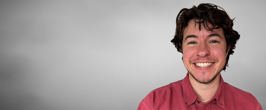 A headshot photo of Noah Levine, smiling, wearing a red collared shirt, against a gray background. 