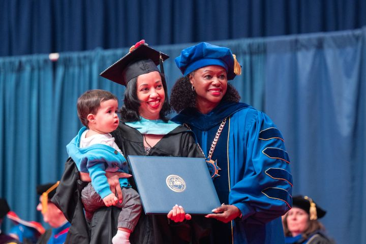 Spring 2026 Commenencement Graduate holding child with Dr. Bell-Jordan