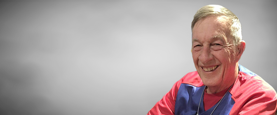 A headshot photo of Frederick O. Flener, Ph.D., smiling, wearing a blue and red jersey, against a gray background.