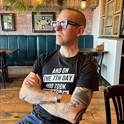 Brandon is seated looking left and wearing a black t-shirt.